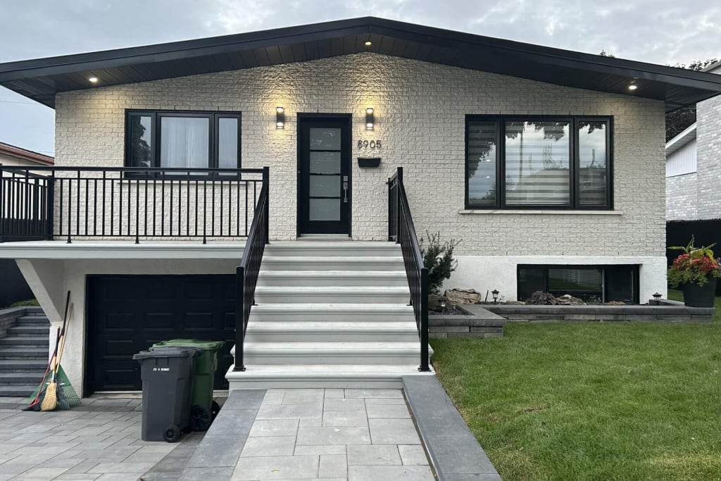 Maison rénovée avec brique peinte au spray, fenêtres noires et escalier moderne à Longueuil.